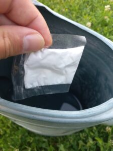 Photo montrant une main qui jette le sachet hydrosoluble de biostimulant dans un arrosoir rempli d'eau